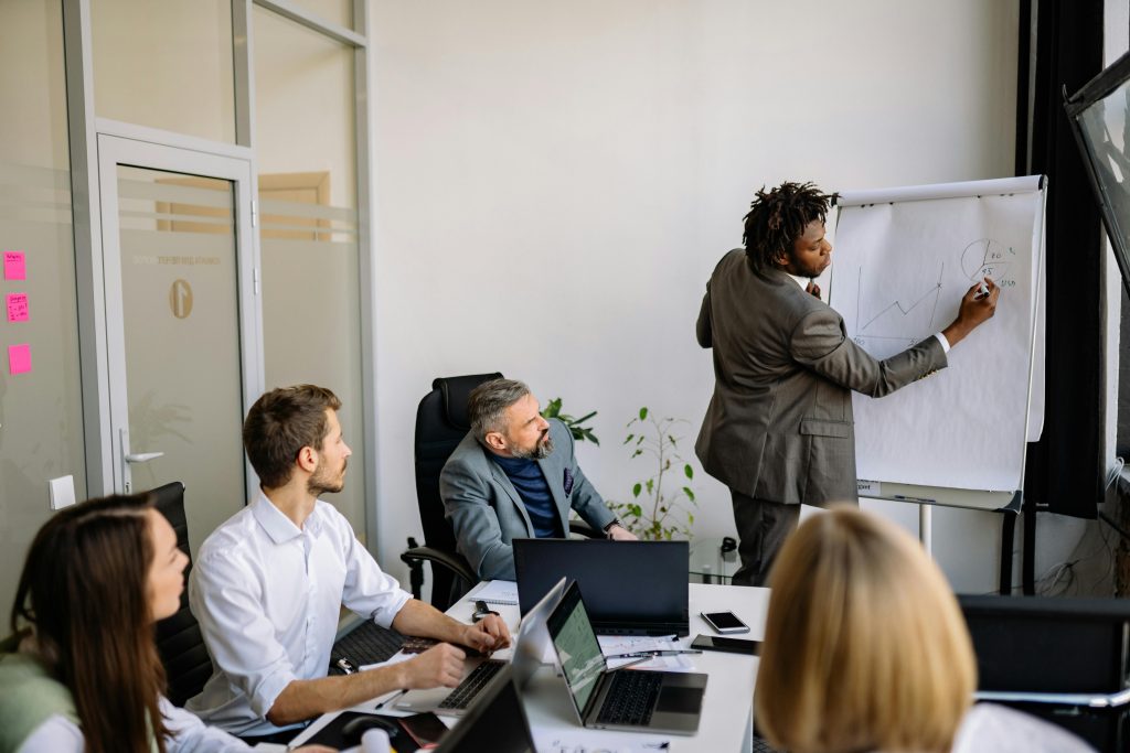 Communities A diverse team in a modern office engaged in a strategic business meeting led by a presenter.